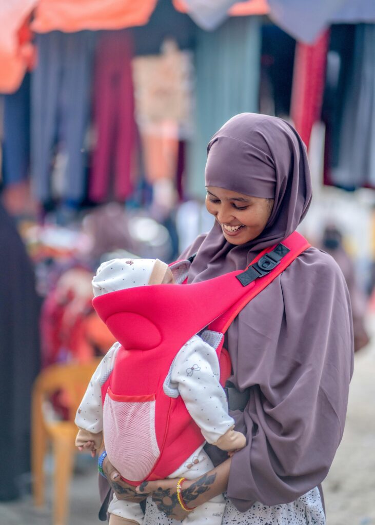 pexels-photo-28808690-28808690 A joyful Somali mother wearing a hijab cradles her baby outdoors in a bustling market in Mogadishu, Somalia.